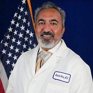 Professional portrait of Dr. Ami Bera wearing a white doctor's coat with an American flag behind him.